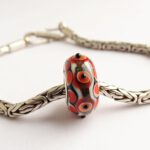 glasbedel met oranjerode stippen en goudsteen