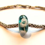 groen turquoise glaskraal met lila bloemen