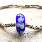 Donkerblauwe glaskraal met 3 lichtgrijze bloemen